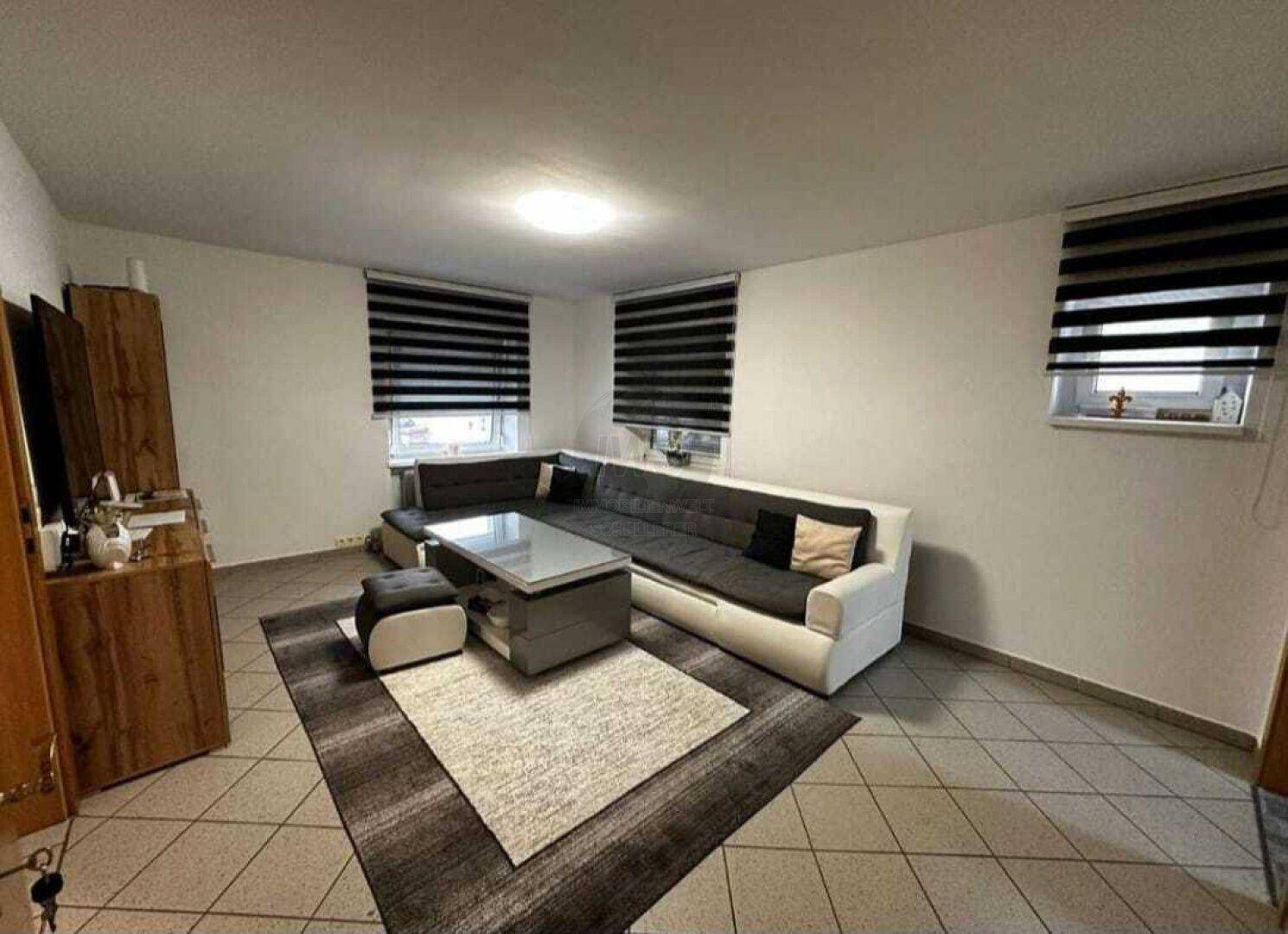 Geräumiges Wohnzimmer mit großem Ecksofa, Couchtisch und Fliesenboden.
