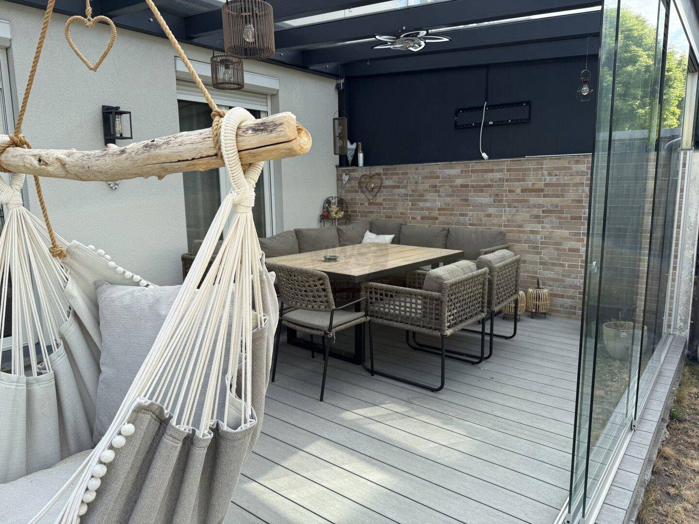 Gemütliche verglaste Terrasse mit bequemen Outdoor-Möbeln und Hängesessel für Entspannung.