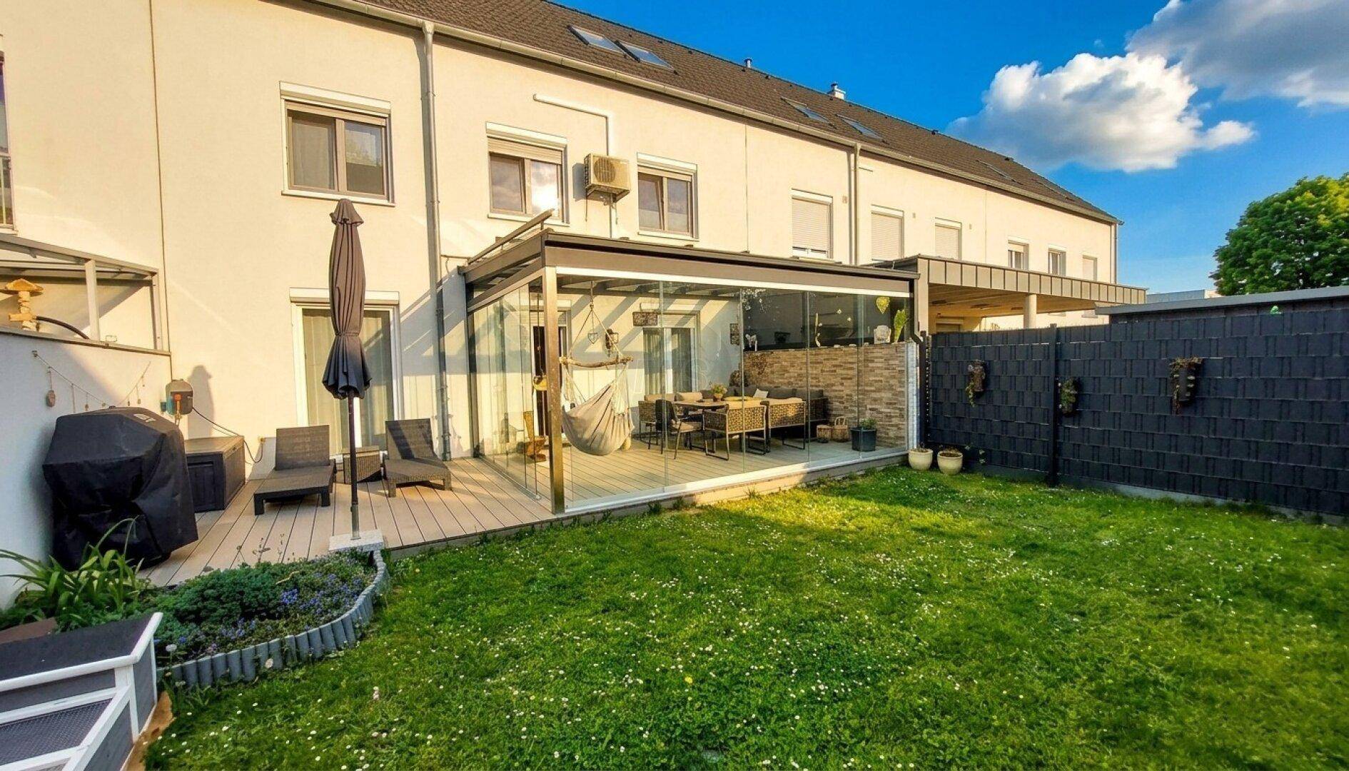Rückansicht des Reihenhauses mit großer verglaster Terrasse und angrenzendem grünen Garten.