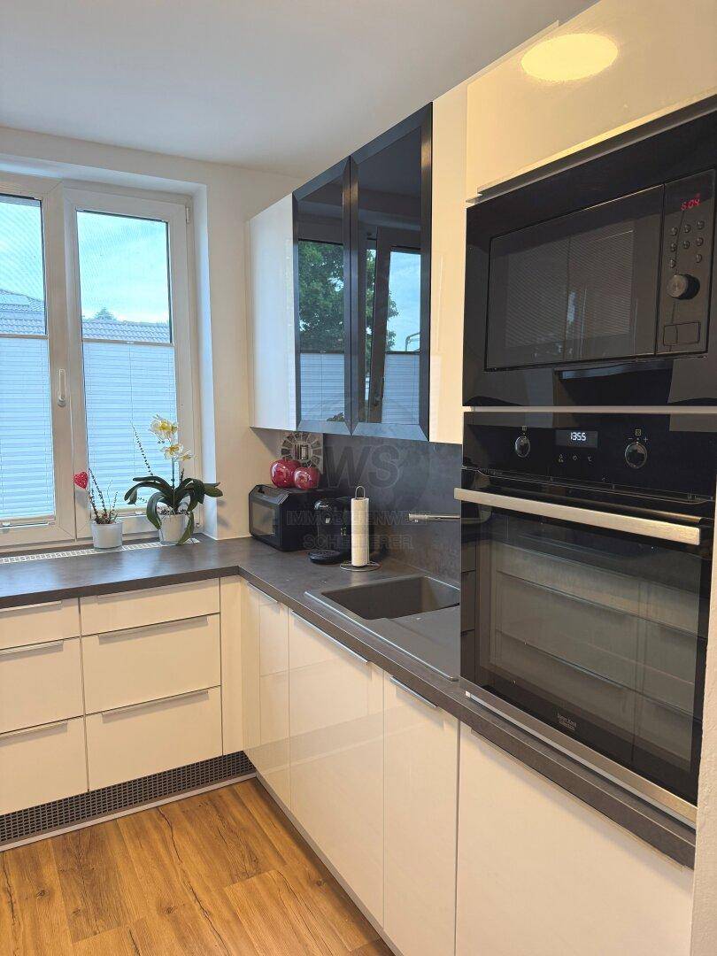 Moderne Küche mit weißen Hochglanzfronten, integriertem Backofen und Mikrowelle.