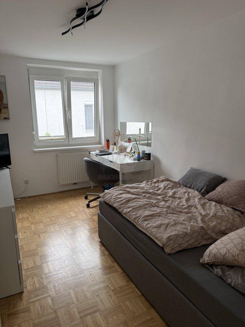 Helles Schlafzimmer mit Parkettboden, Schreibtisch und Fenster für viel Tageslicht.