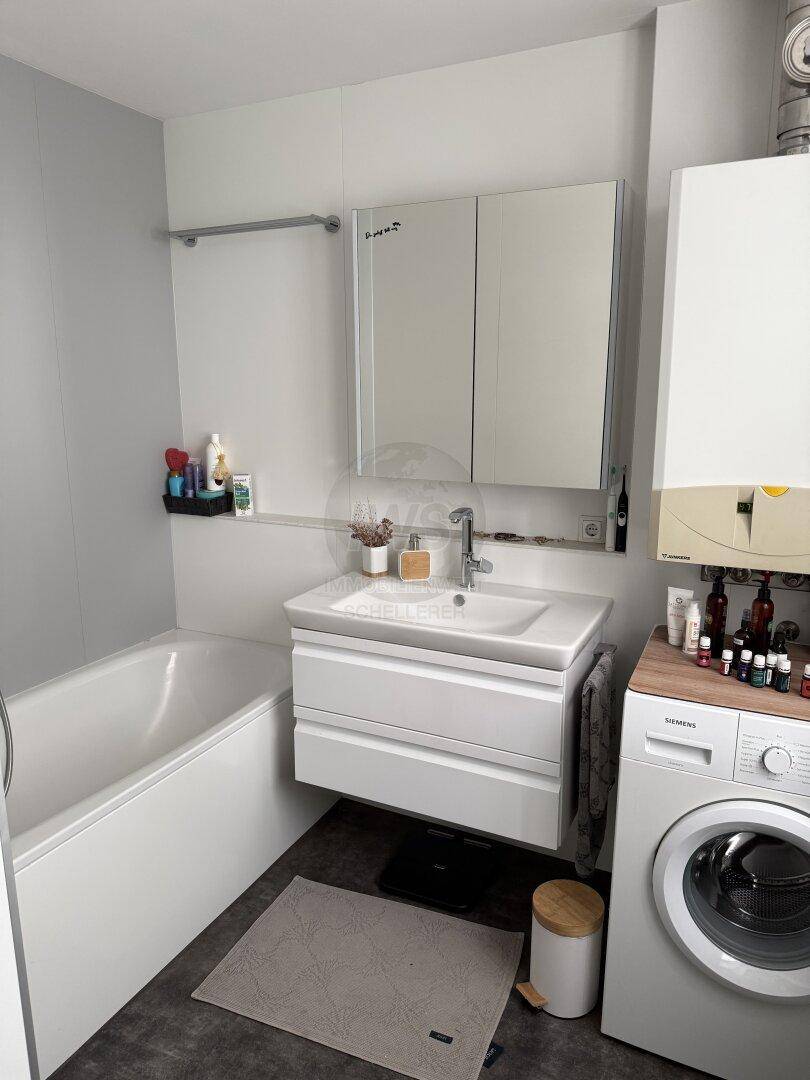 Modernes Badezimmer mit Badewanne, Waschbecken, Spiegelschrank und Waschmaschine.