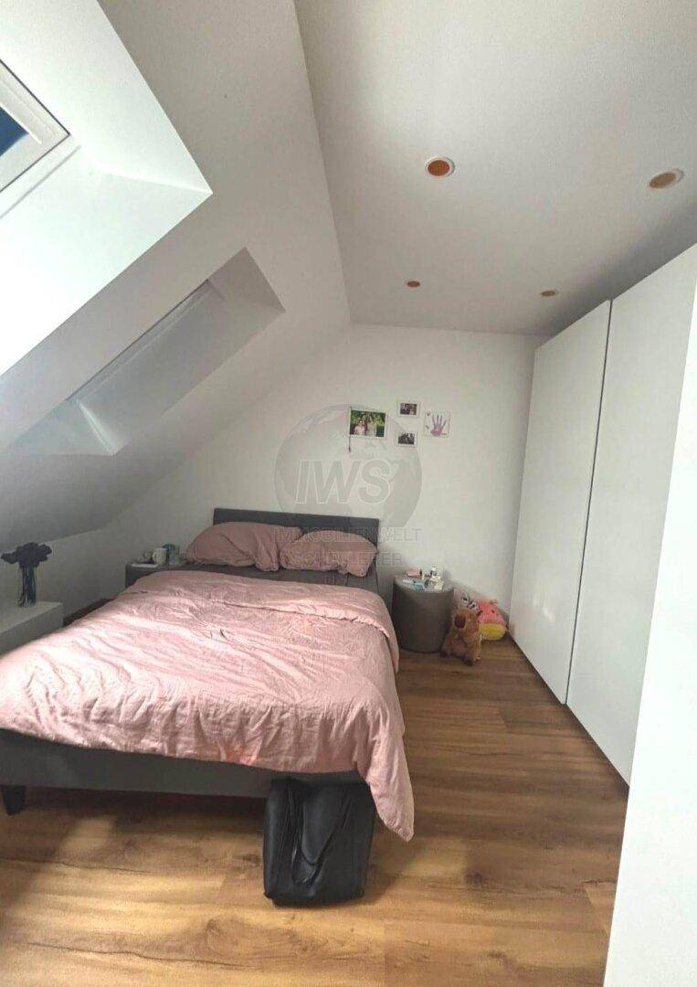 Gemütliches Schlafzimmer im Dachgeschoss mit Bett, Dachfenster und schrägen Wänden.
