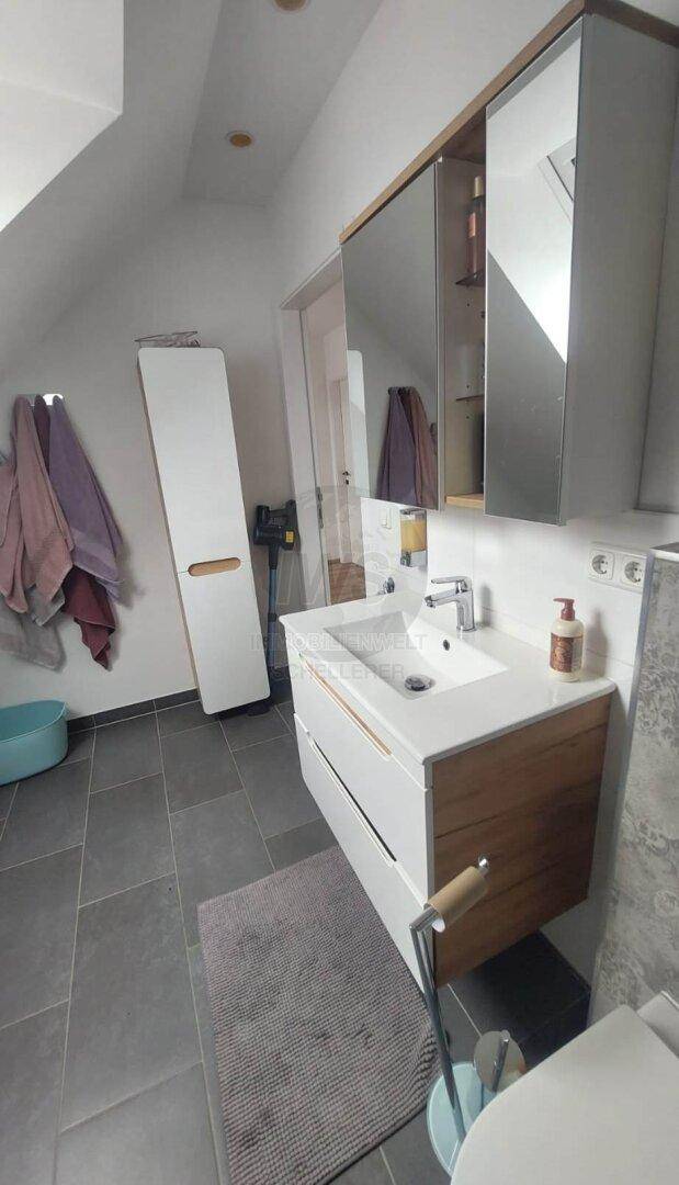 Badezimmer im Dachgeschoss mit Waschbecken, Spiegelschrank und schrägen Wänden.
