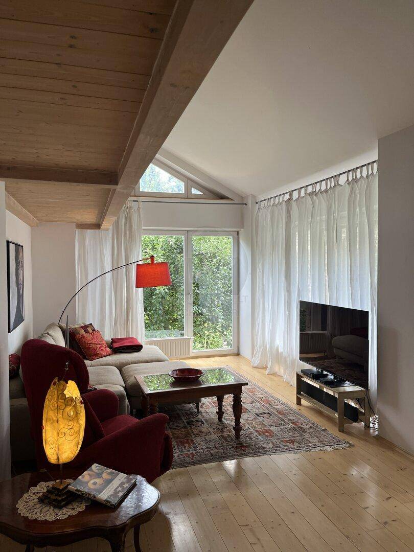 Lichtdurchflutetes Wohnzimmer mit Holzboden, gemütlicher Sitzecke und großen Fenstern.