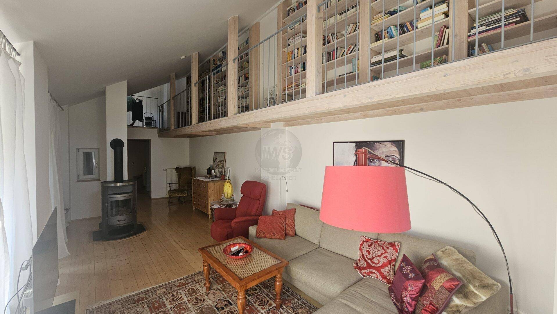 Geräumiges Wohnzimmer mit Kaminofen, Sofa und einer Galerie mit Bücherregalen.