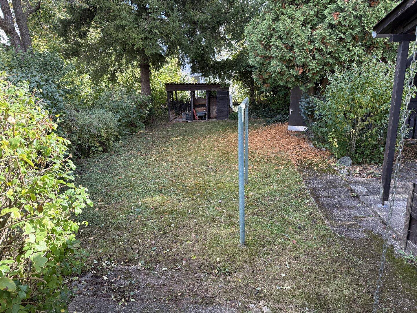 Großer, grüner Garten mit Rasenfläche und einem kleinen Geräteschuppen im Hintergrund.