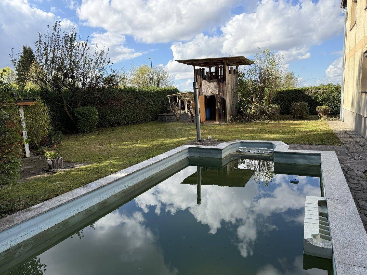 Gartenbereich mit einem eingelassenen Pool, Rasenfläche und einem hölzernen Spielhaus.