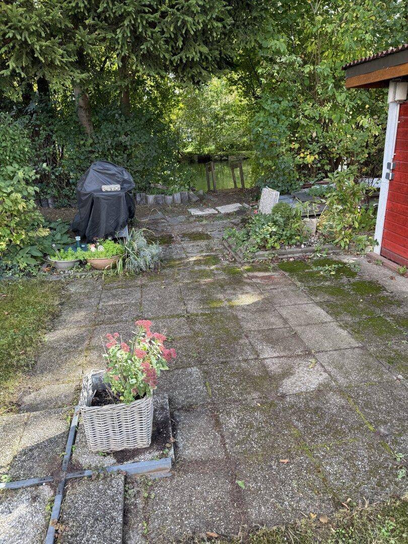 Gepflasterte Terrasse mit Grillbereich und Pflanzen, die zum Wasser führt.