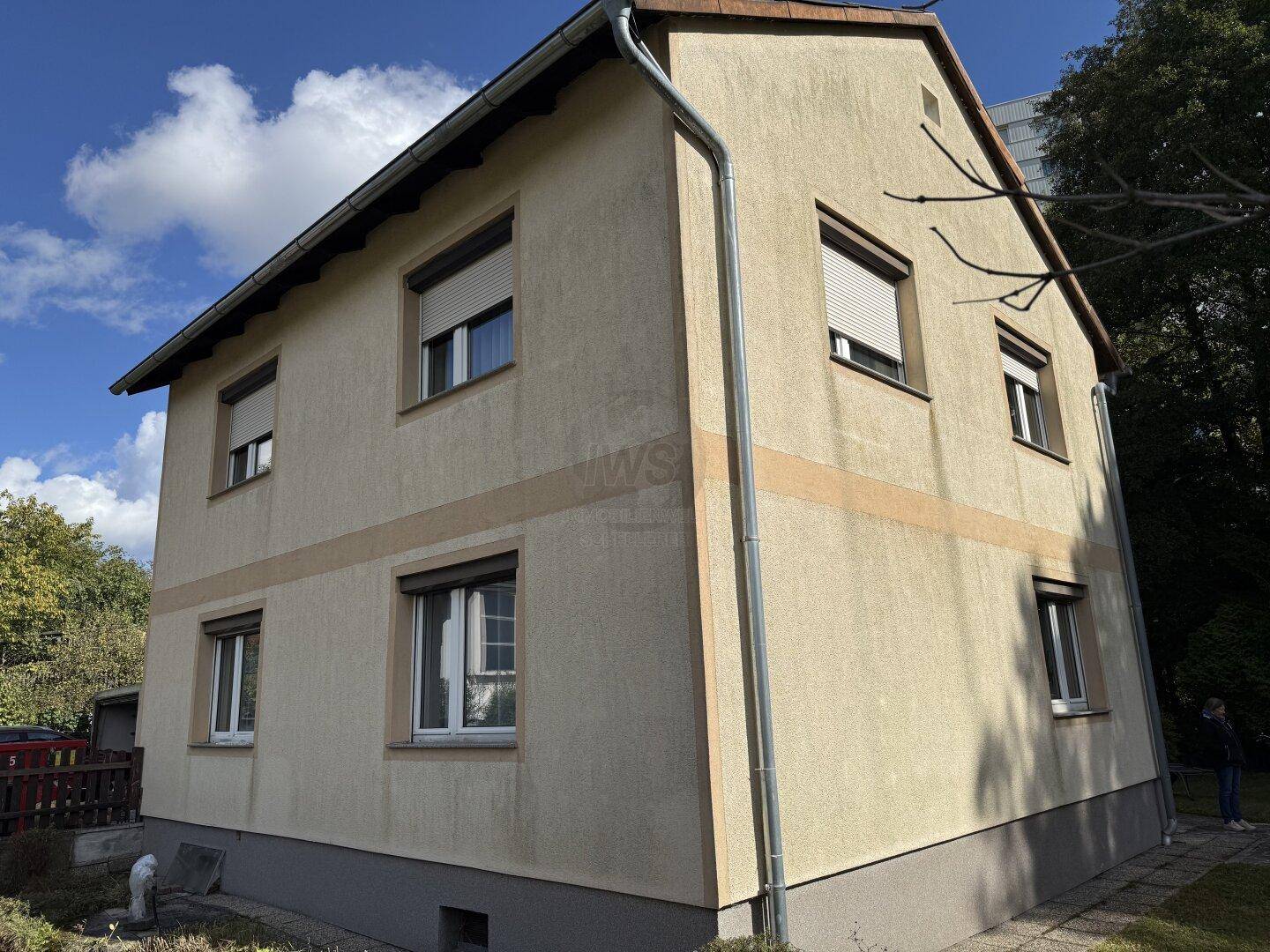Seitenansicht des Hauses mit beiger Fassade, Rollläden und einem kleinen Gartenbereich.