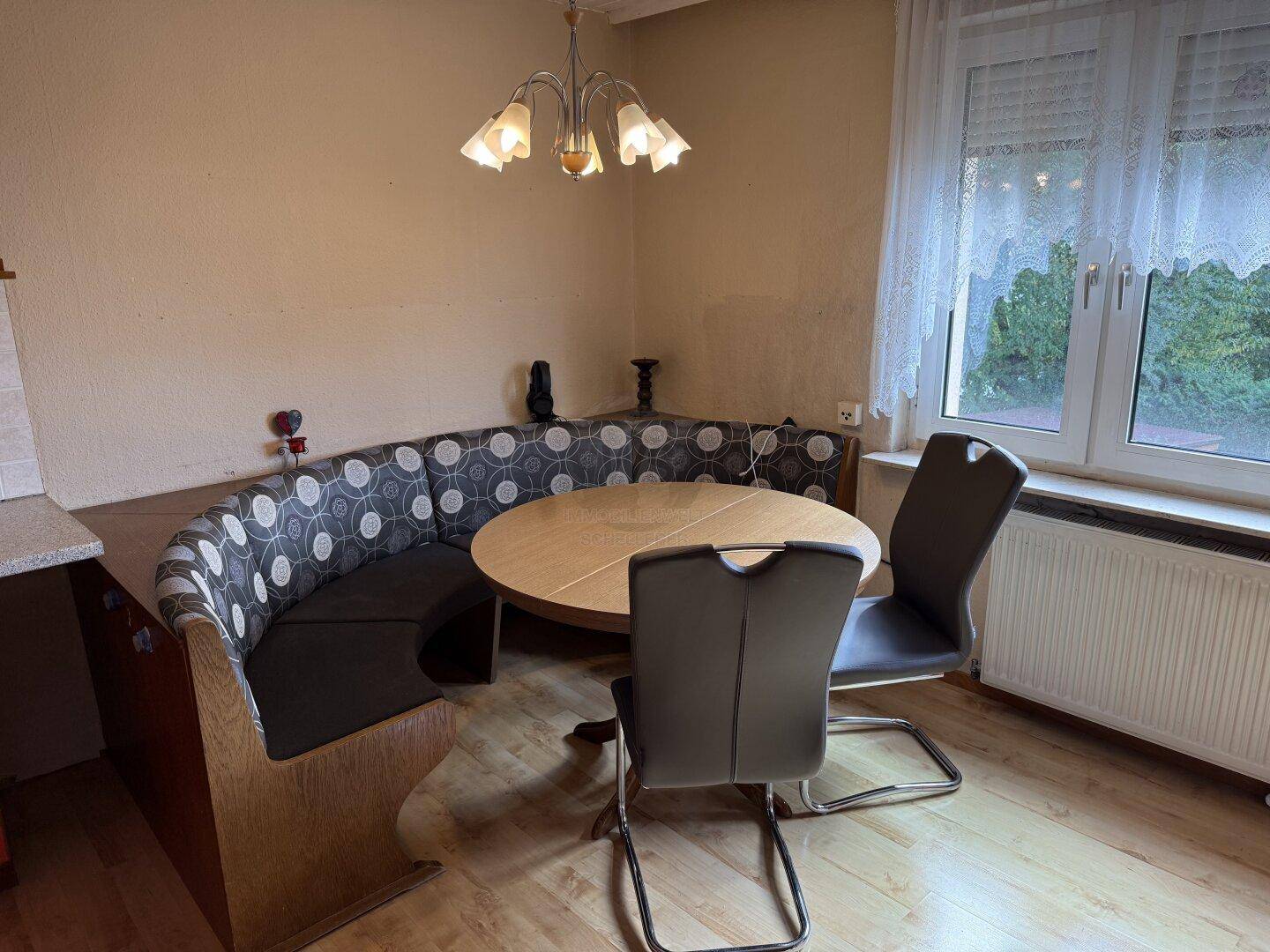 Heller Essbereich mit runder Holztafel und einer gepolsterten Eckbank am Fenster.