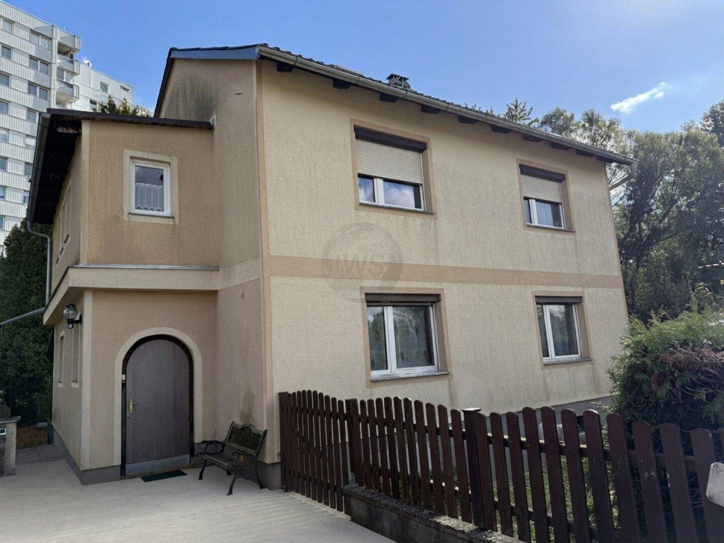 Beige verputztes Einfamilienhaus mit Rollläden und einem kleinen Vorgarten.