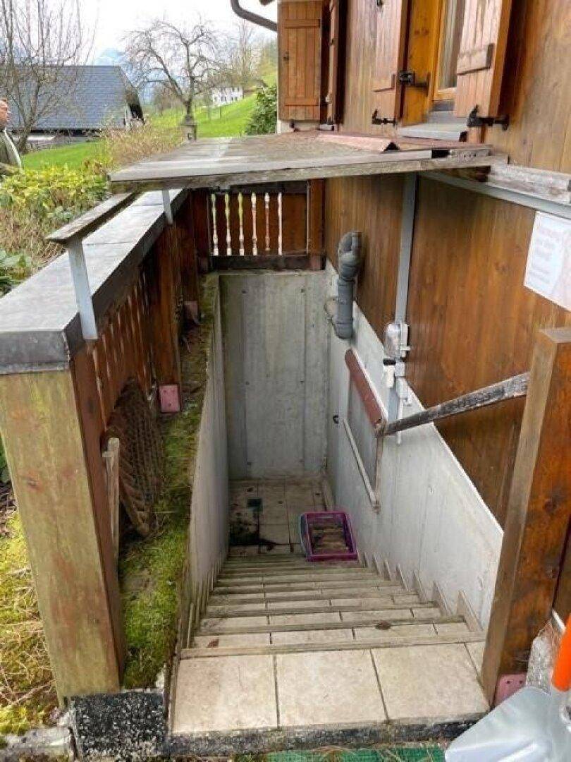 Außentreppe führt hinunter zum Kellereingang, umgeben von Holzvertäfelung und Betonwänden.