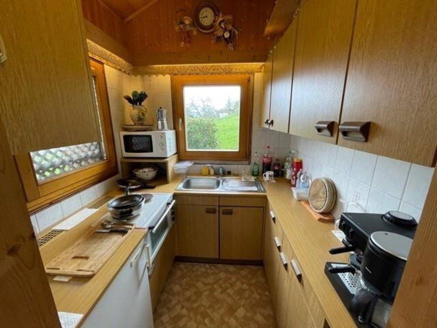 Kleine, rustikale Küche mit Holzschränken, weiß gefliestem Spritzschutz und Blick ins Grüne.