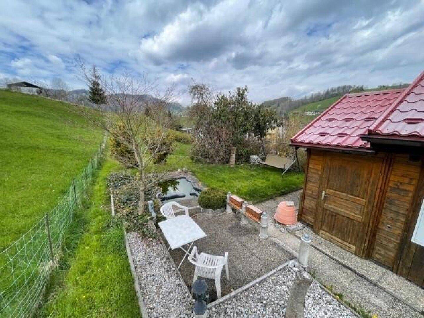 Gepflegter Gartenbereich mit Terrasse, kleinem Teich und dem charmanten Holzhaus im Hintergrund.