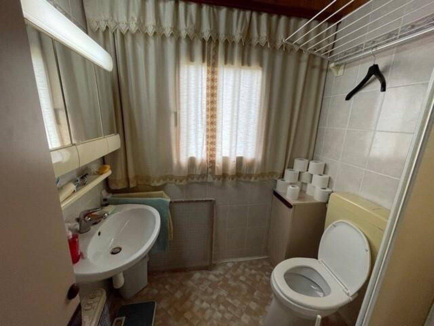 Einfaches Badezimmer mit WC, Waschbecken und Fenster, ausgestattet mit funktionalen Elementen.