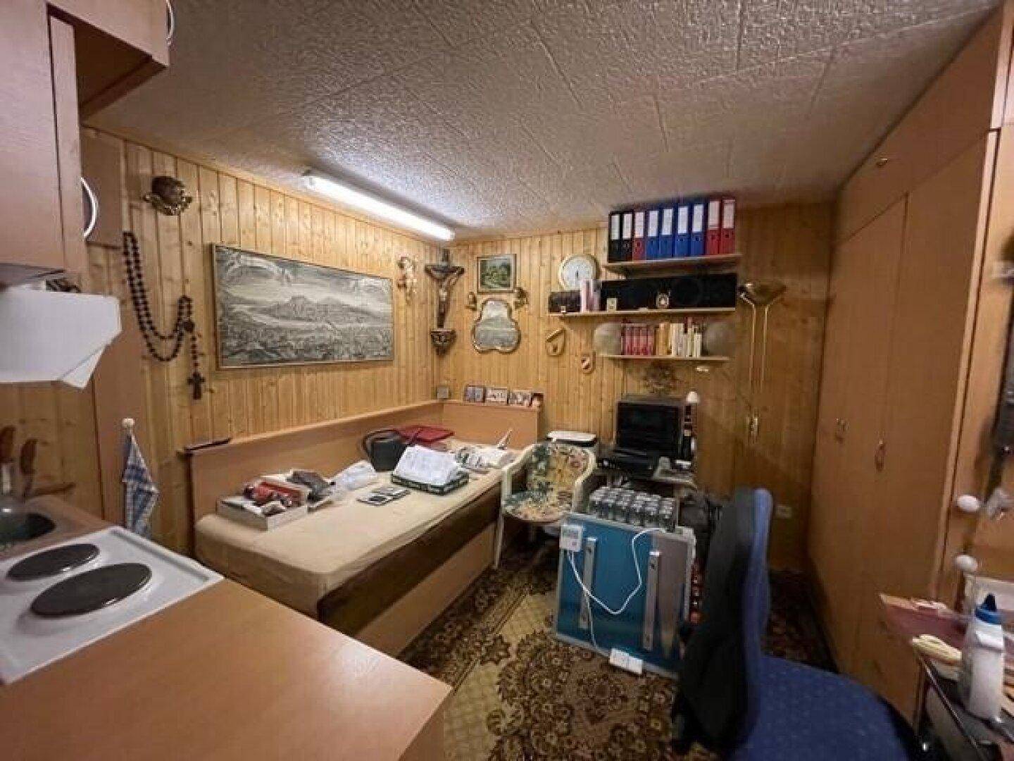 Rustikaler Mehrzweckraum im Untergeschoss mit Holzvertäfelung, Bett und kleiner Kochnische.
