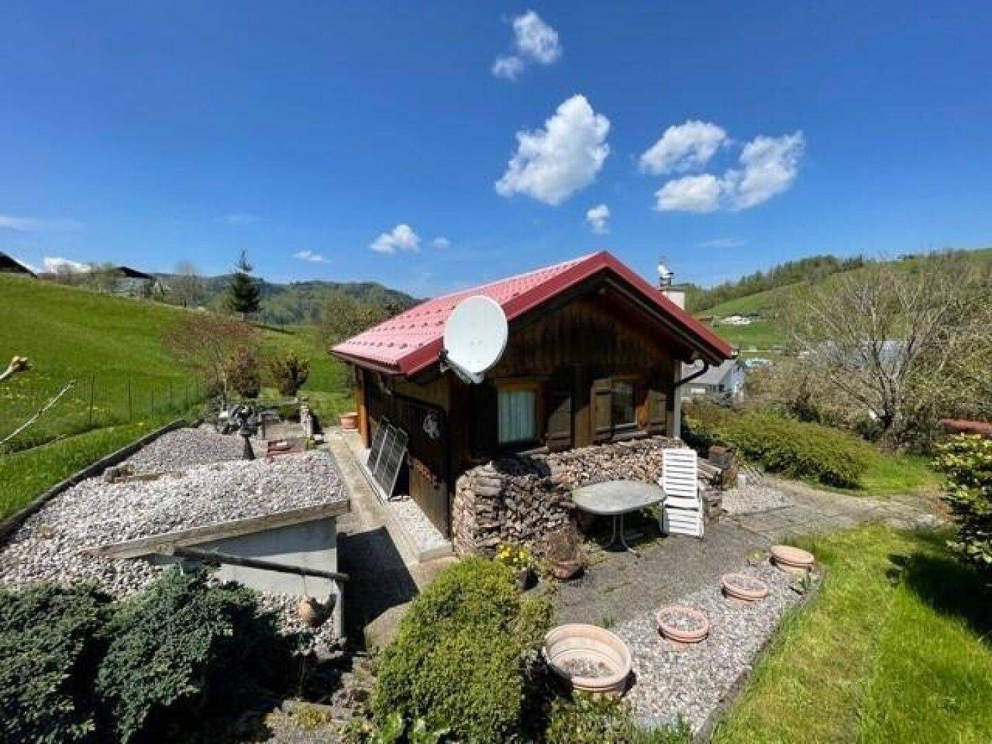 Charmantes Holzhaus mit rotem Dach, umgeben von einem gepflegten Garten mit Kiesflächen und Grün.