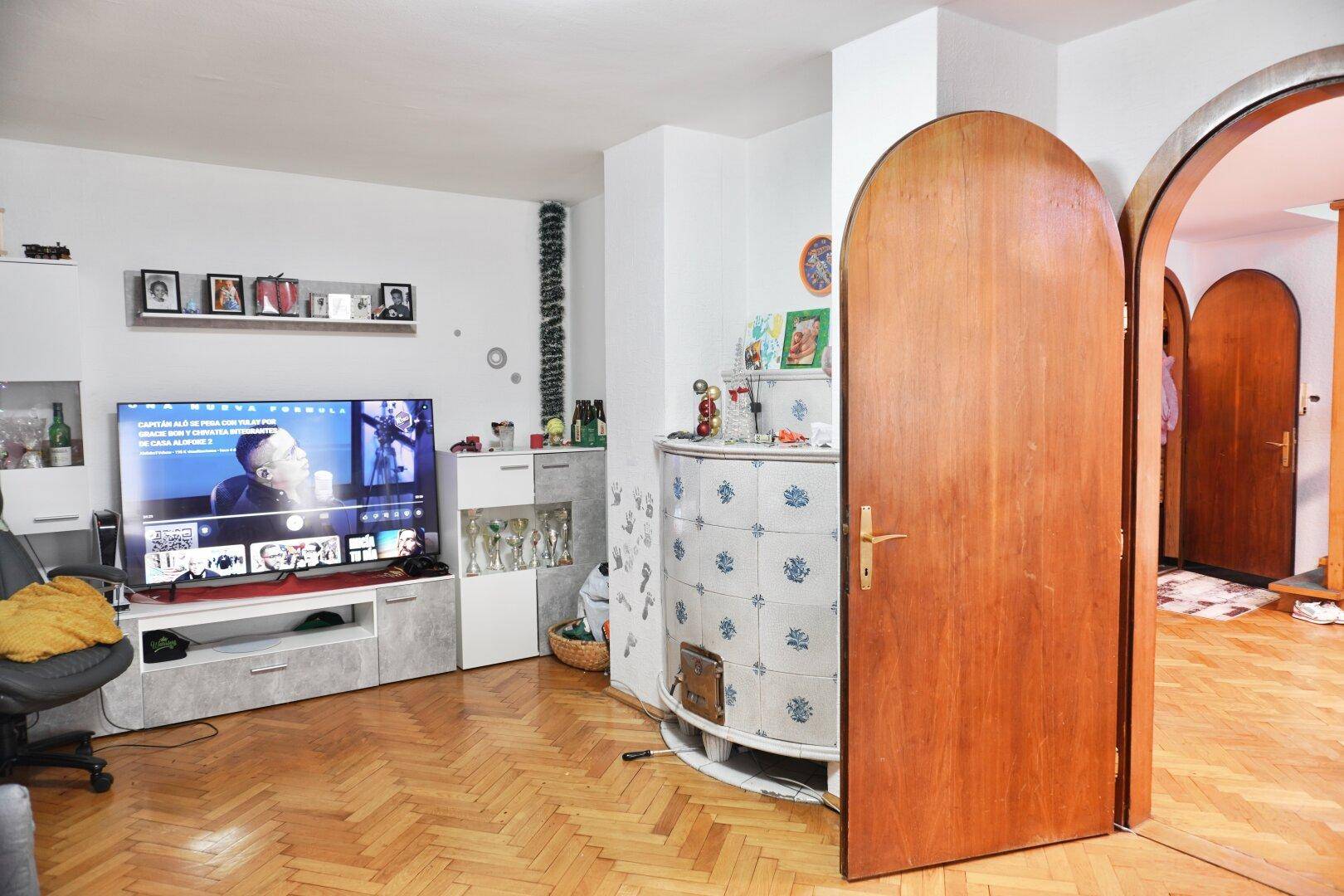 Wohnzimmer mit Fernseher, elegantem Kachelofen und charmanten Rundbogentüren.