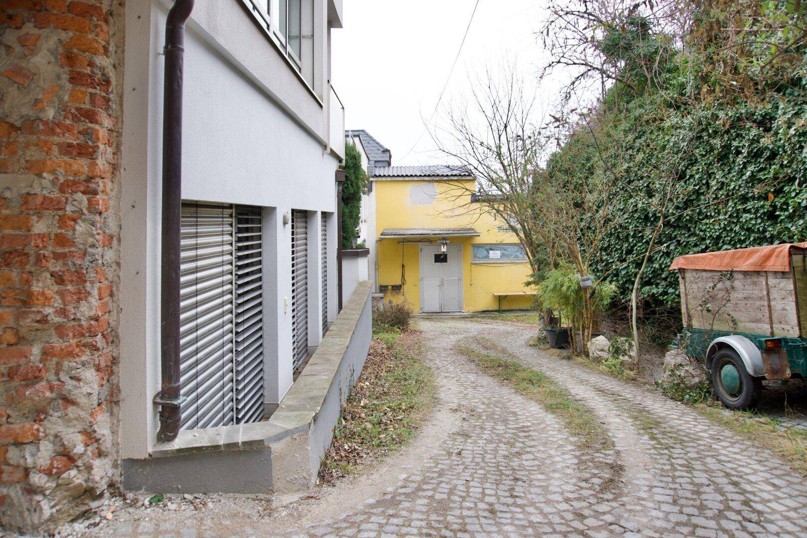 Zufahrt zu einem gelben Gebäude mit Ziegelmauer und üppiger Vegetation.