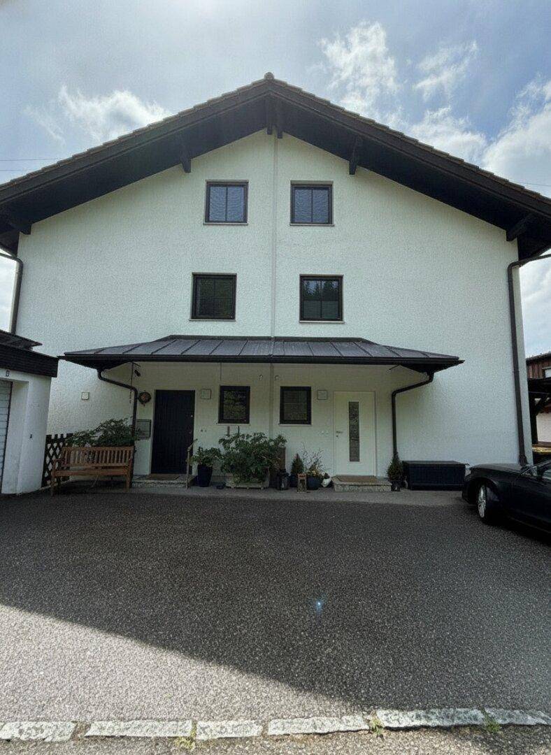Weißes Wohnhaus mit Satteldach, überdachtem Eingangsbereich und einer Einfahrt zur Garage.