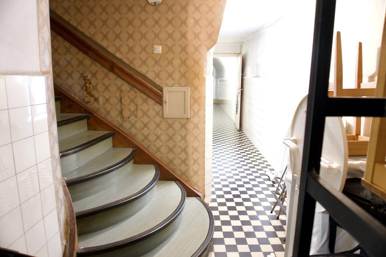 Treppenhaus mit gemusterter Tapete und angrenzendem Flur mit schwarz-weiß gefliestem Boden.