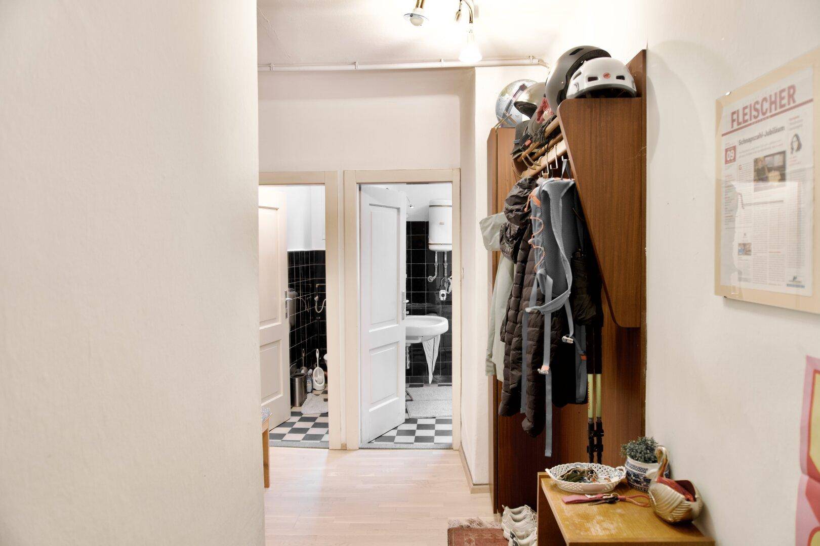 Heller Flur mit Garderobe und Blick auf ein Badezimmer mit schwarz-weiß gefliestem Boden.