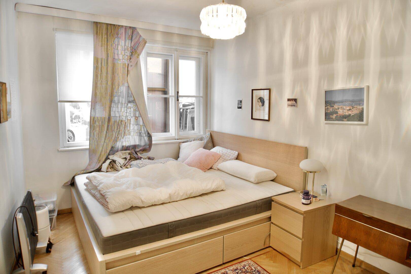 Gemütliches Schlafzimmer mit hellem Holzbett, Nachttisch und Fenster für natürliches Licht.