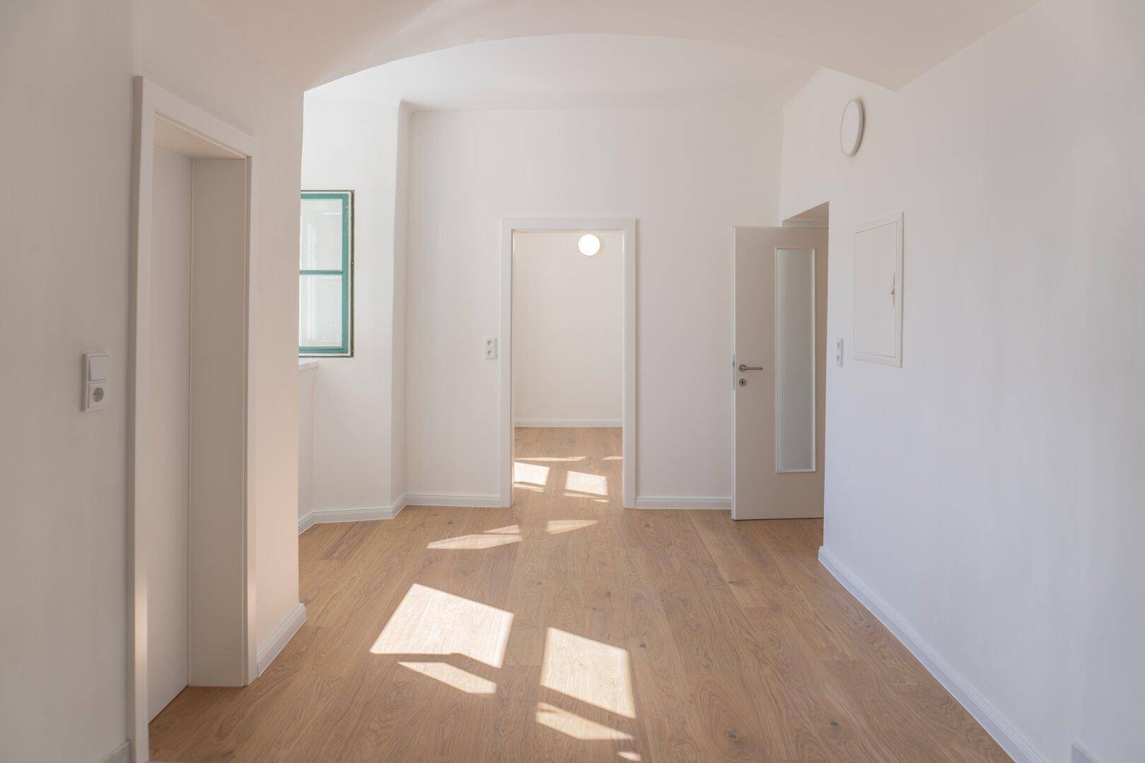 Heller Flur mit Holzboden und viel Tageslicht, der zu weiteren Räumen führt.