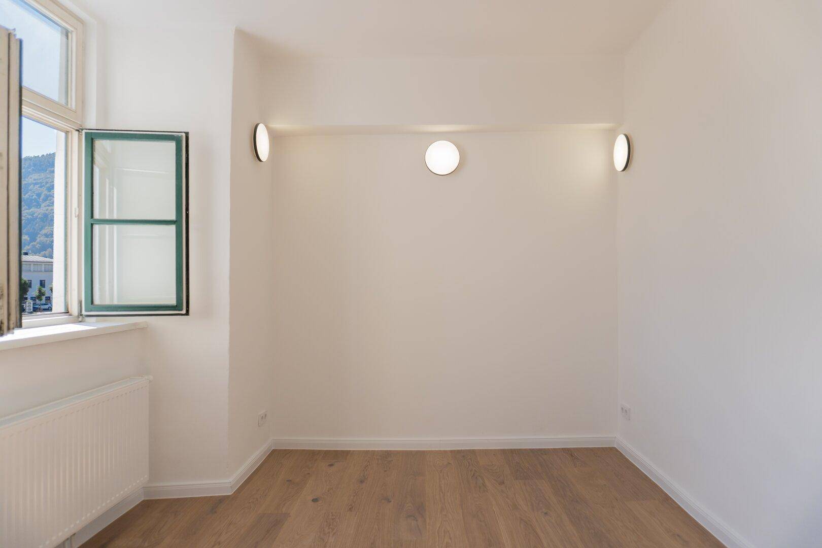 Leeres Zimmer mit Holzboden und modernen Wandleuchten, bereit zur individuellen Gestaltung.