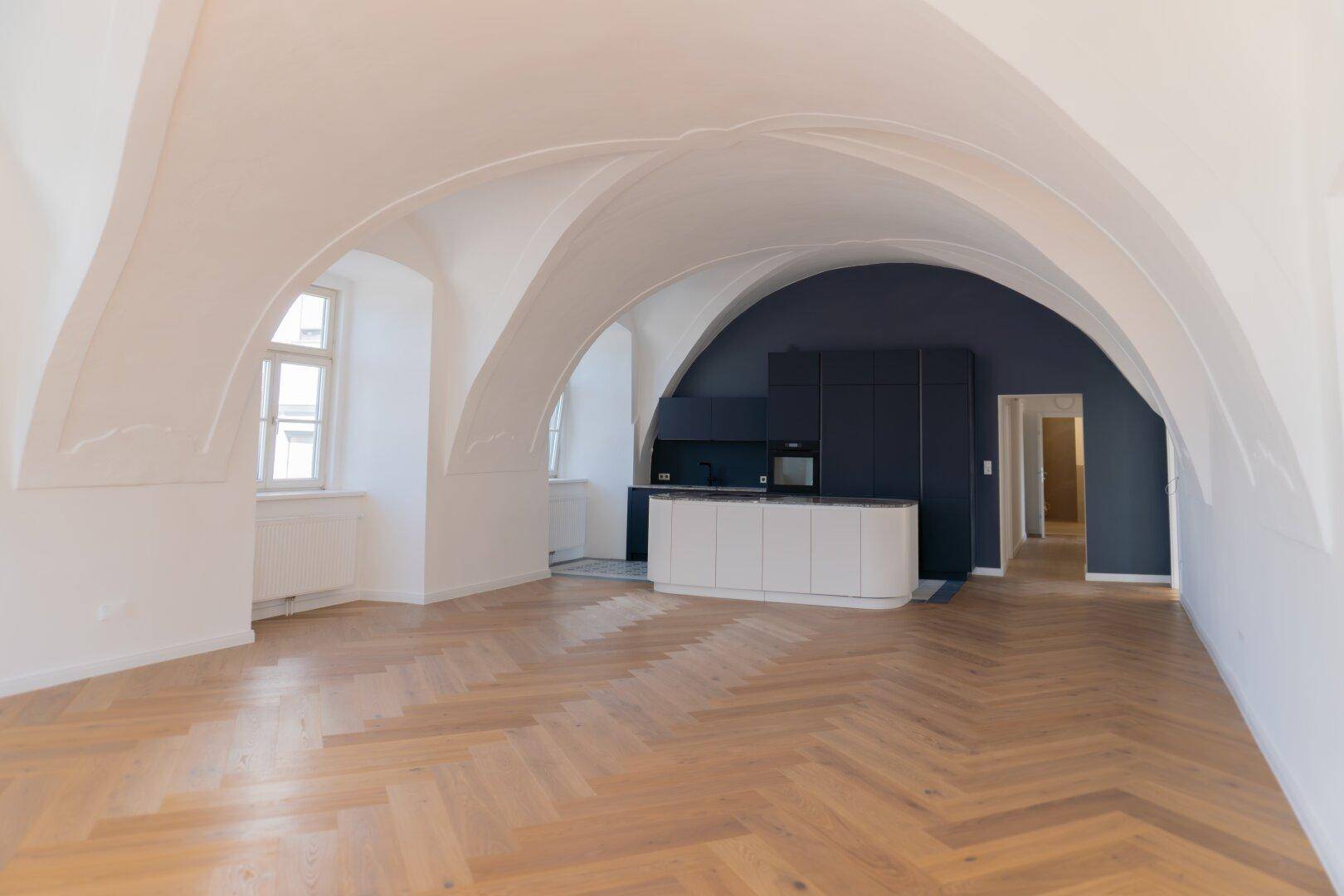 Offener Wohnbereich mit moderner Einbauküche, Gewölbedecken und Fischgrätparkett.