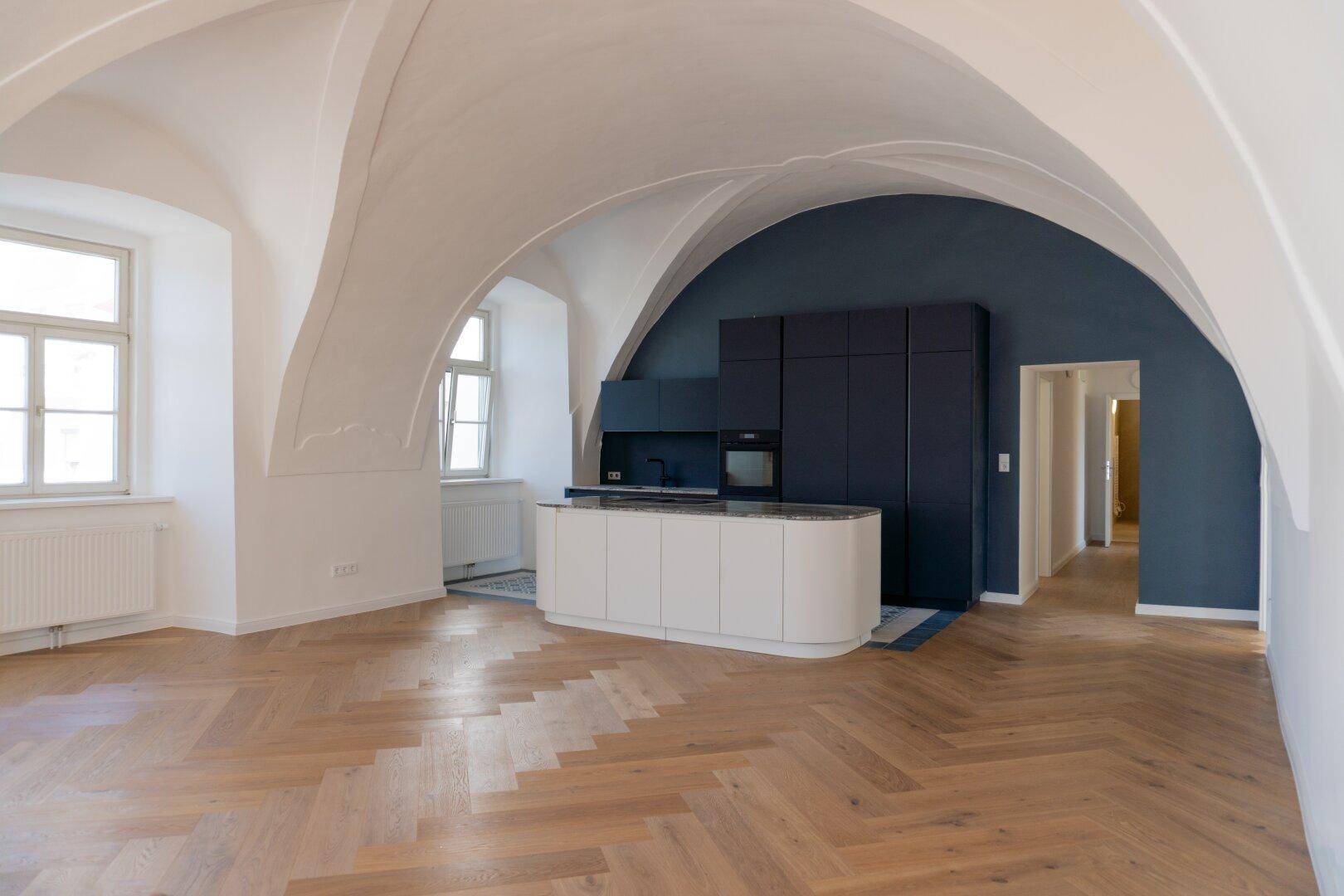 Moderner offener Wohnbereich mit integrierter Küche, Gewölbedecken und elegantem Fischgrätparkett.