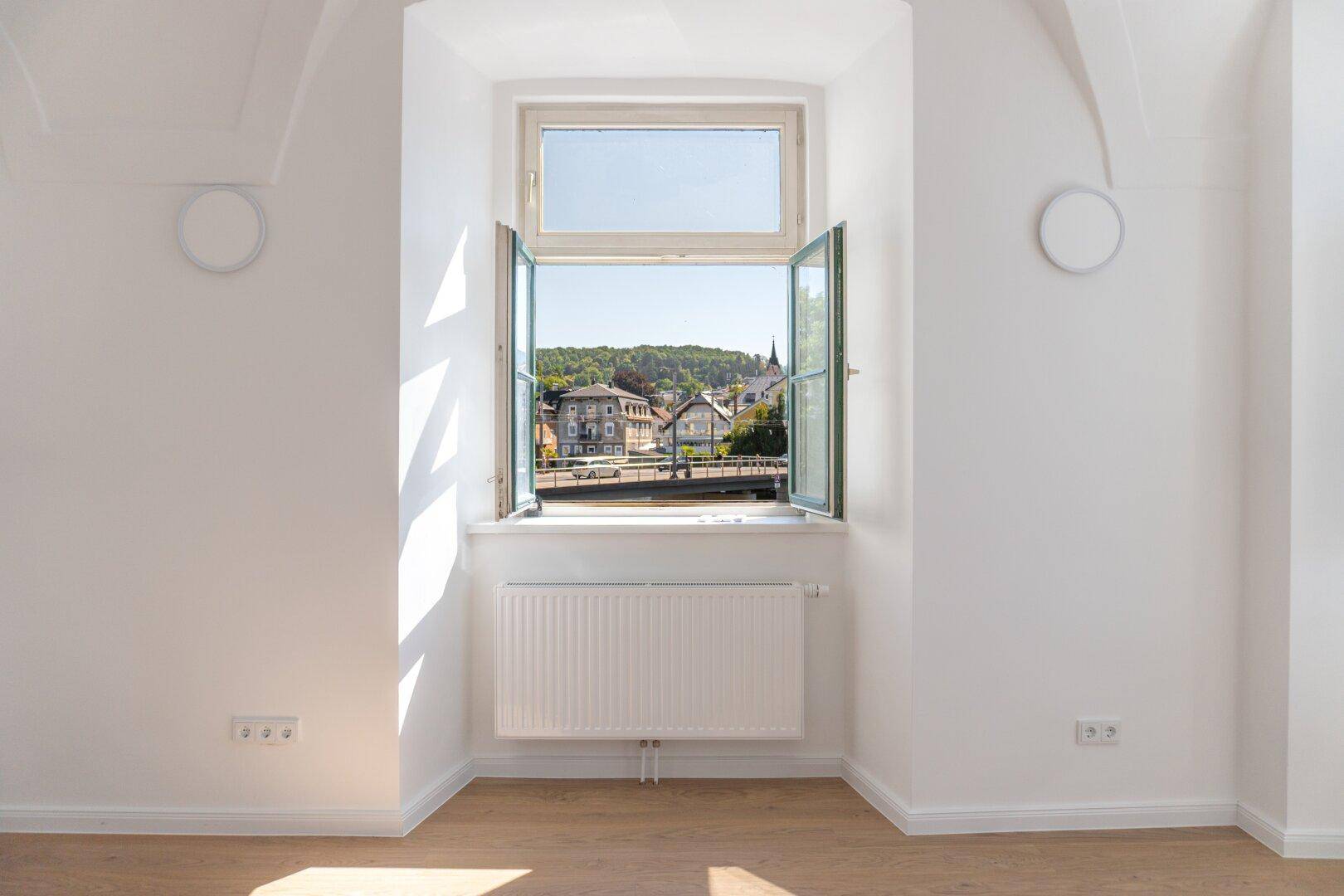 Helles Zimmer mit Fenster und Blick auf die Stadt und den Fluss, ausgestattet mit Heizkörper.