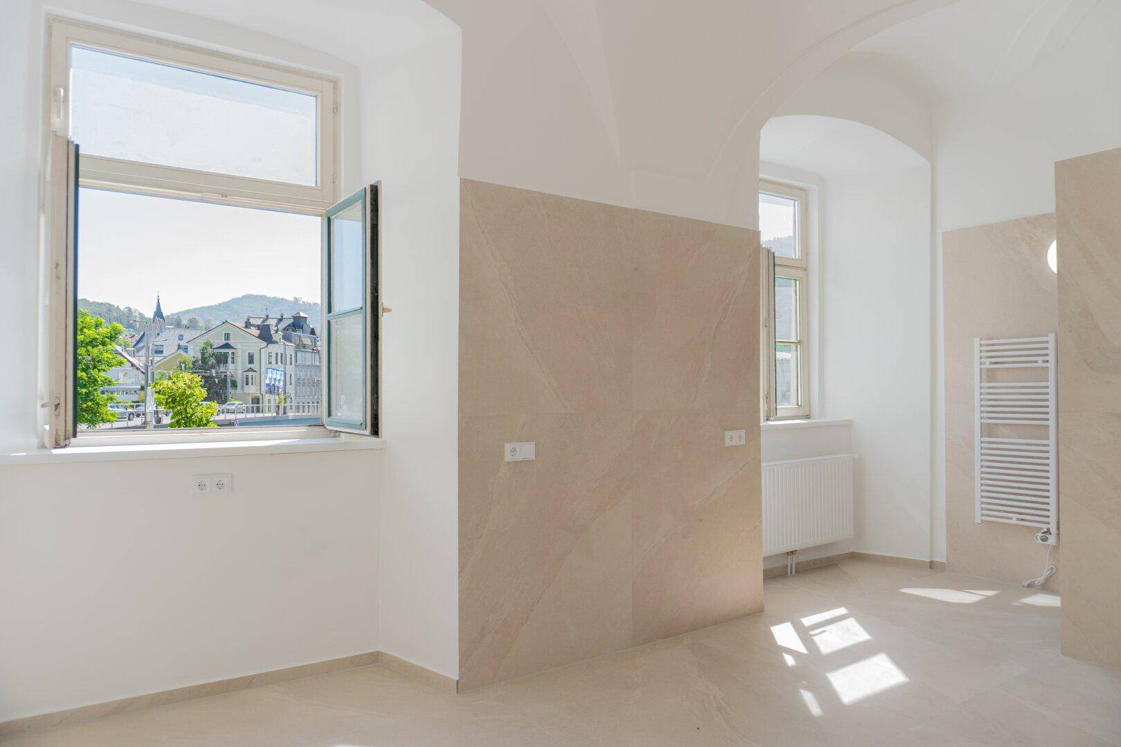 Geräumiges Badezimmer mit hellen Fliesen, Fenster und Heizkörper, bereit für die Installation.