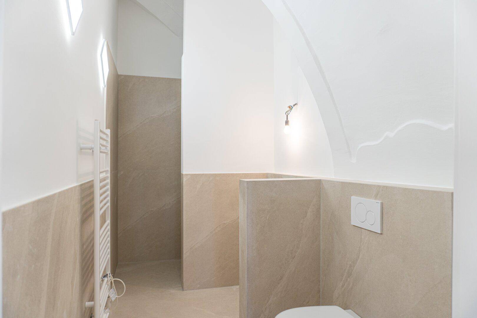Modernes Badezimmer mit hellen Fliesen, Wand-WC und Heizkörper, in neuwertigem Zustand.
