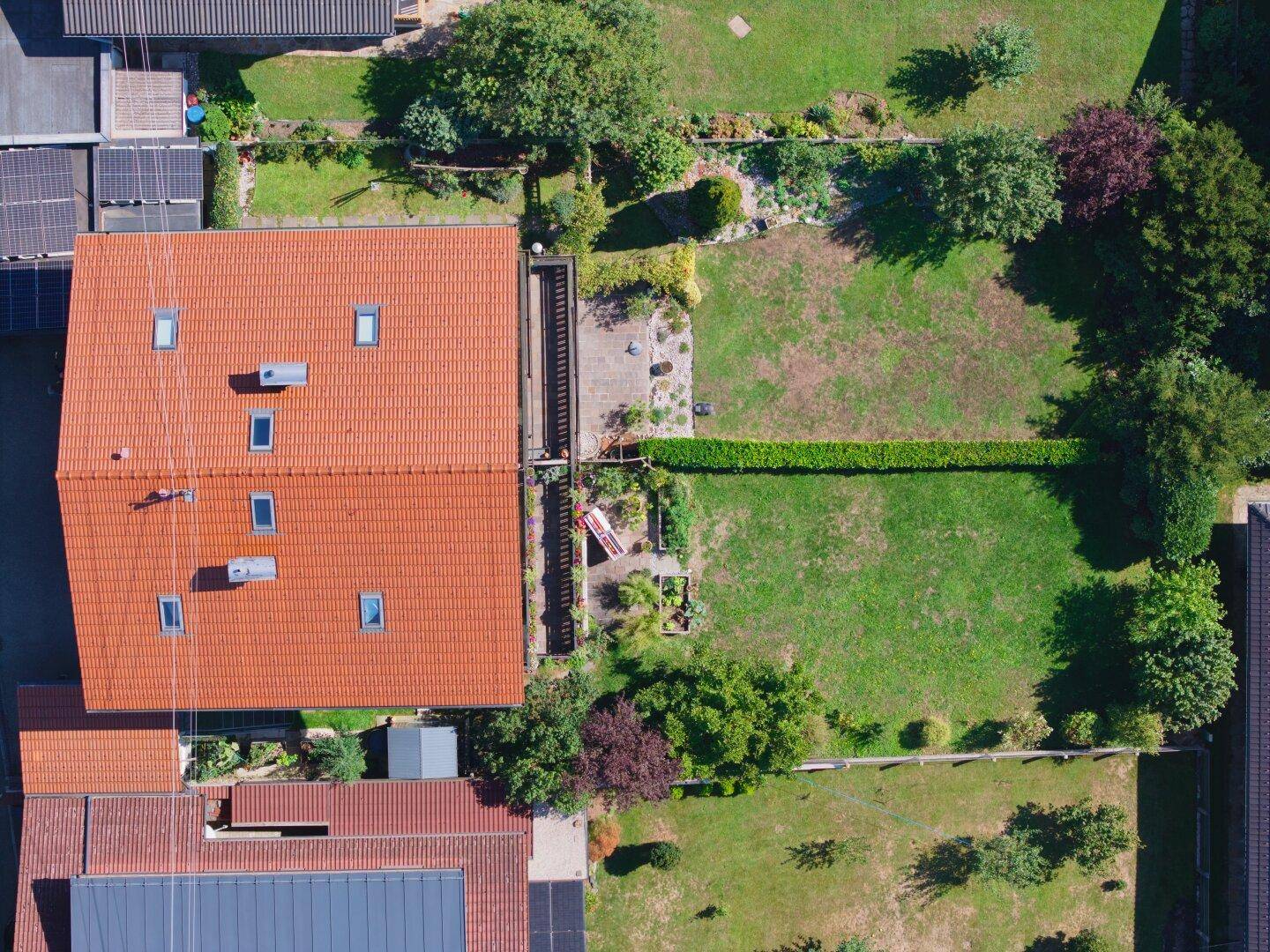 Draufsicht auf ein Wohnhaus mit Ziegeldach, Dachfenstern und einem gepflegten Gartenbereich.