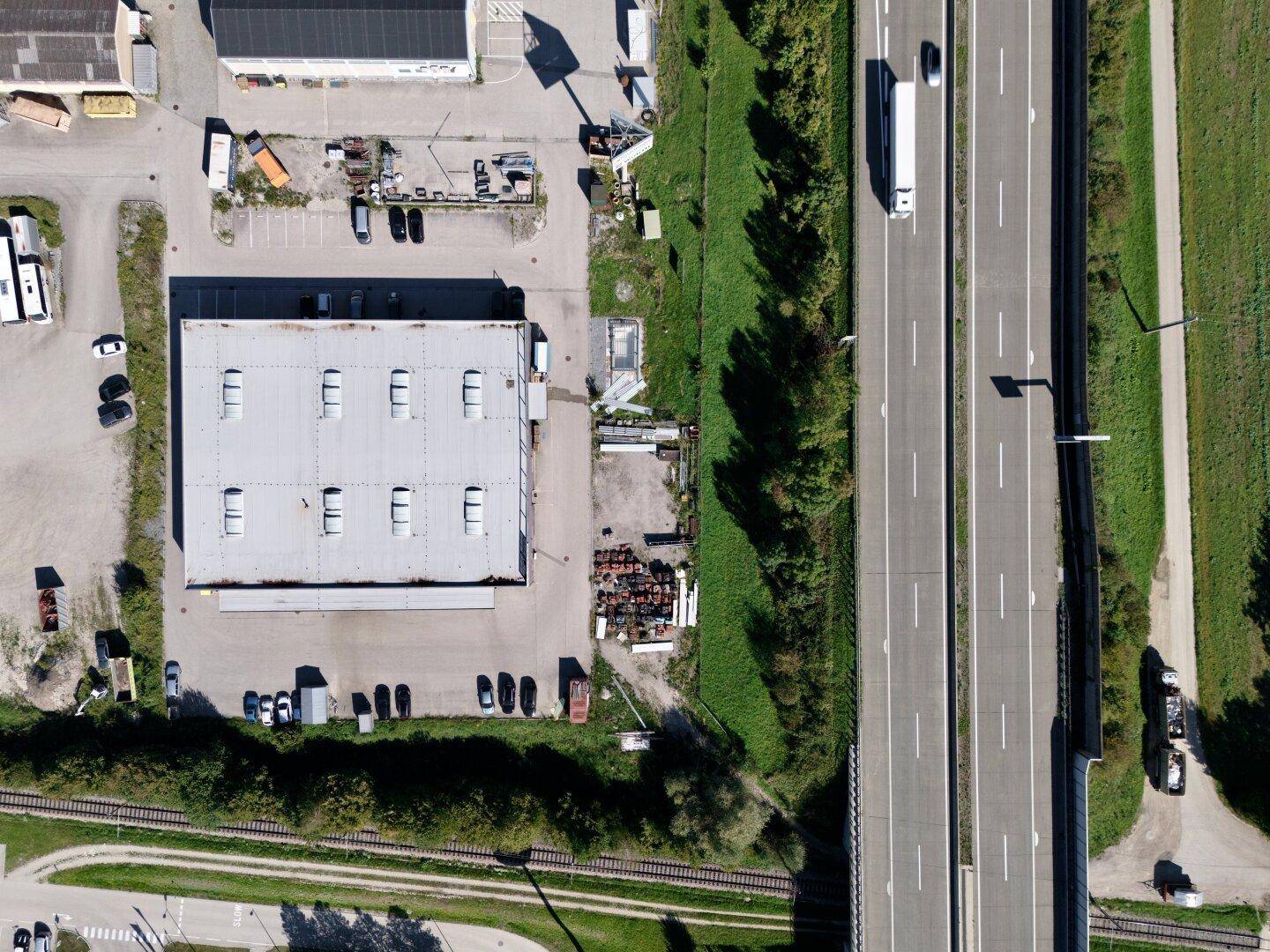 Senkrechte Luftaufnahme eines Gewerbegebäudes mit Flachdach und der Autobahn daneben.