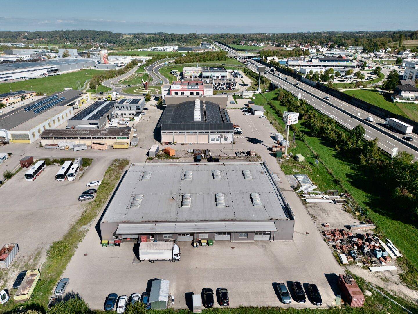 Übersicht des Gewerbegebiets mit mehreren Hallen, Parkflächen und der angrenzenden Autobahn.
