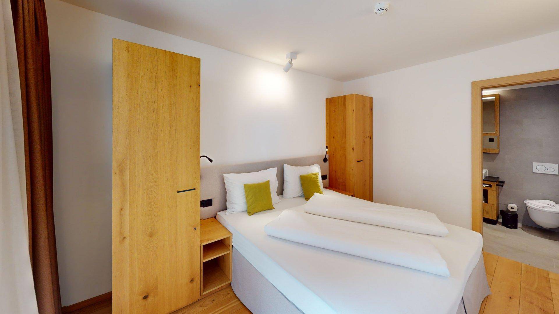 Gemütliches Schlafzimmer mit Holzboden, Doppelbett und direktem Zugang zu einem modernen Badezimmer.