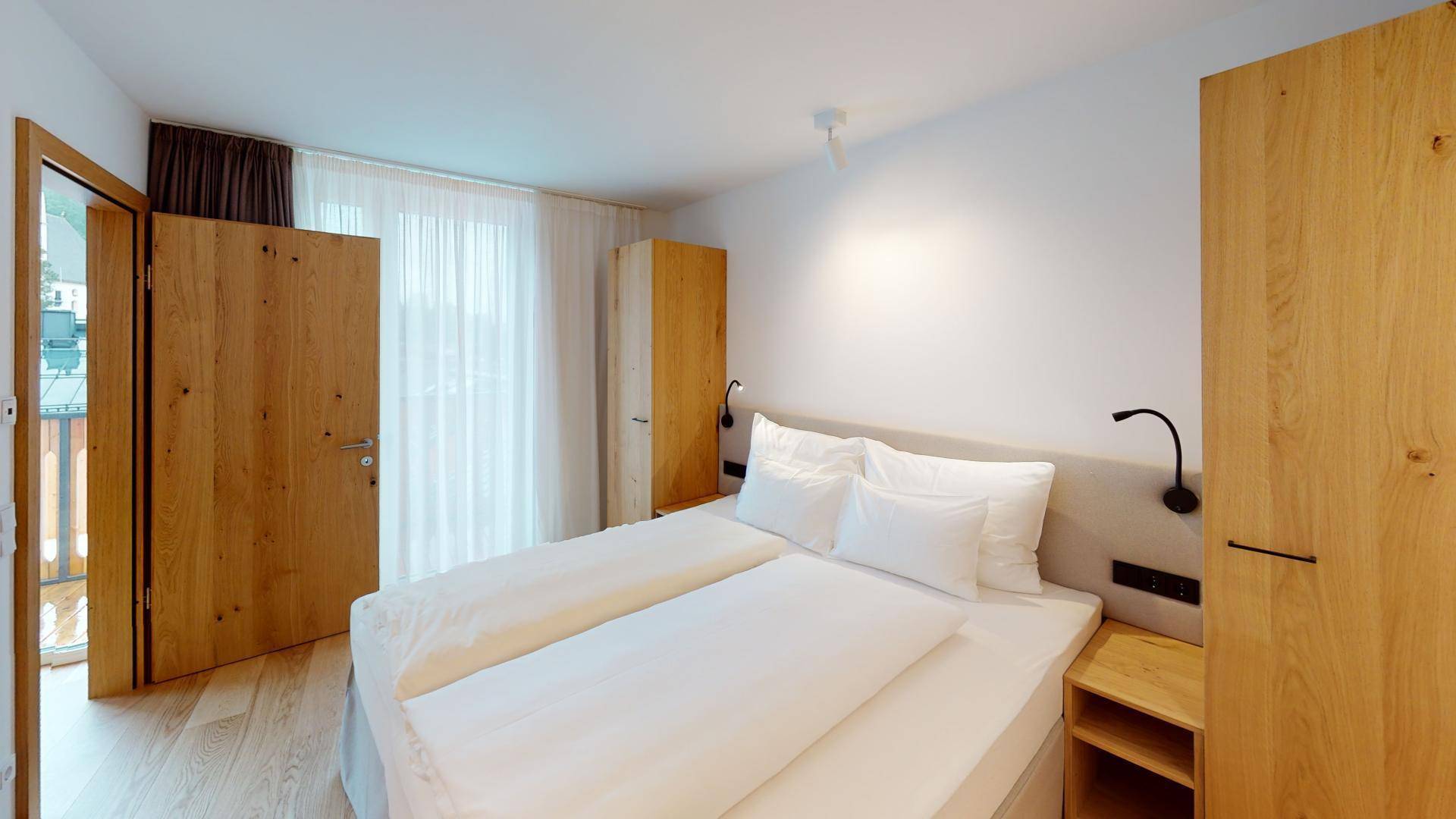 Helles Schlafzimmer mit Holzboden, Doppelbett und direktem Zugang zu einem Balkon.