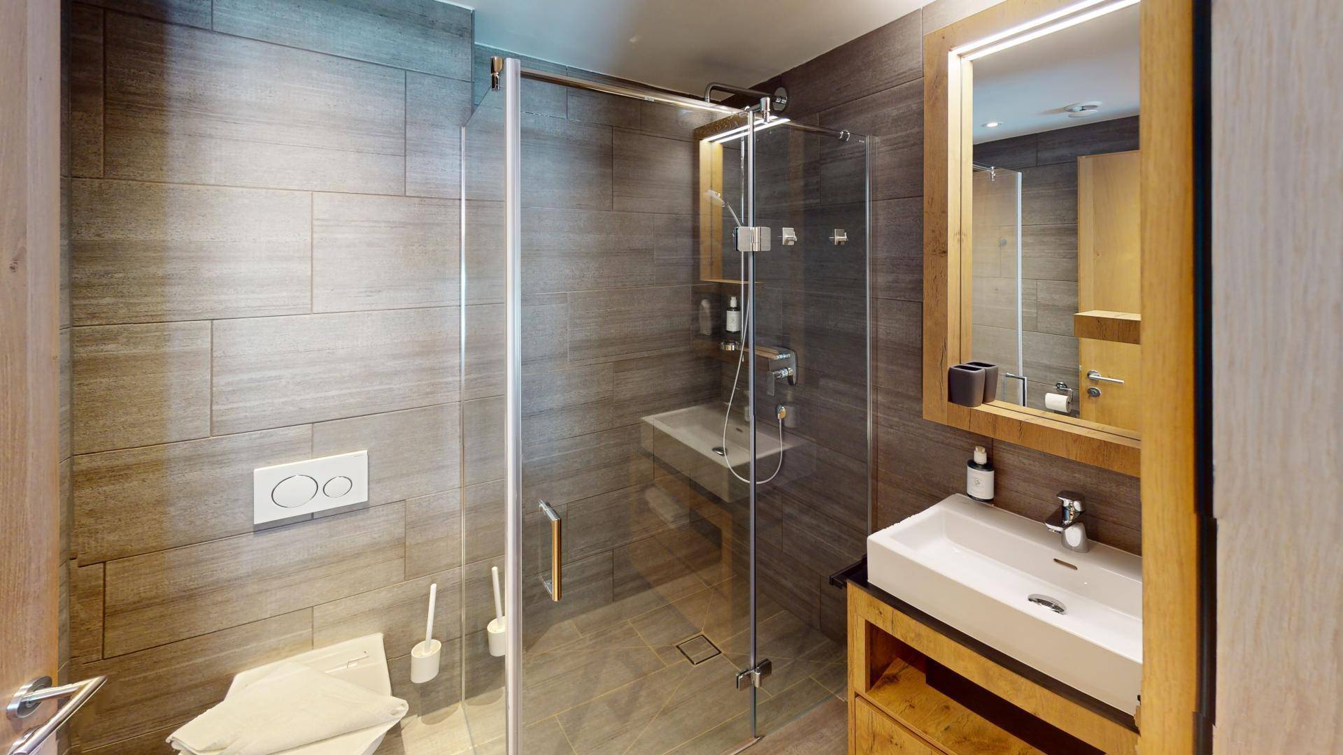 Modernes Badezimmer mit begehbarer Dusche, grauen Fliesen und Holzwaschtisch.