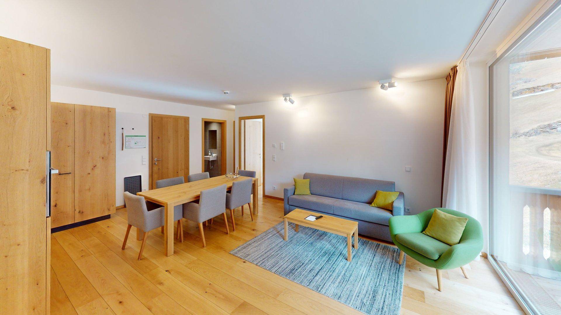 Heller Wohn- und Essbereich mit Holzboden, modernem Sofa und Zugang zum Balkon mit Bergblick.