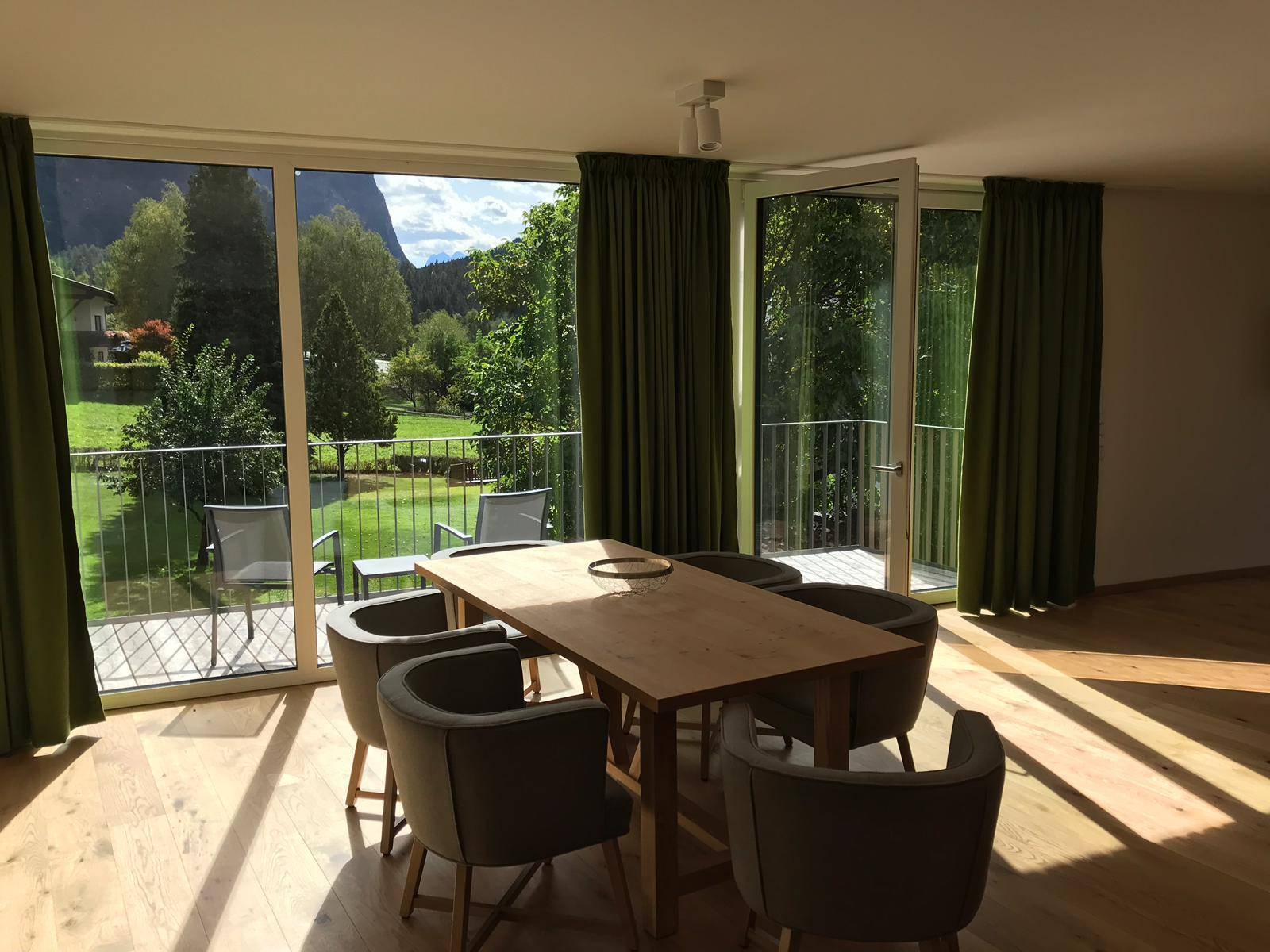 Lichtdurchfluteter Essbereich mit Holztisch, bequemen Stühlen und Zugang zu einem Balkon mit Bergblick.