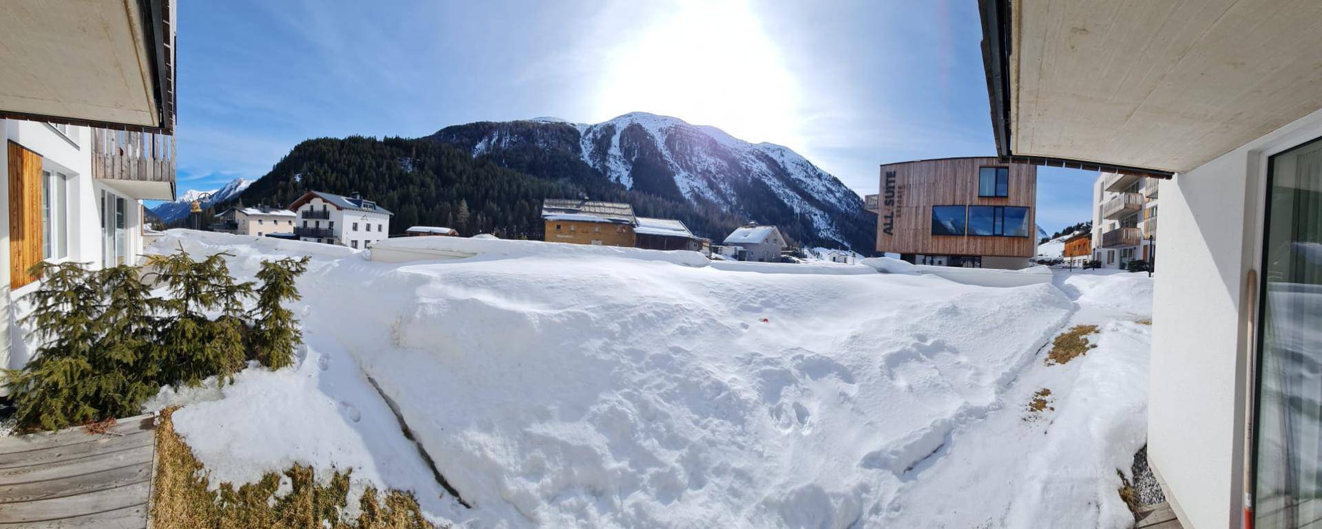 Panoramablick auf die verschneite Berglandschaft und umliegende Gebäude an einem sonnigen Wintertag.