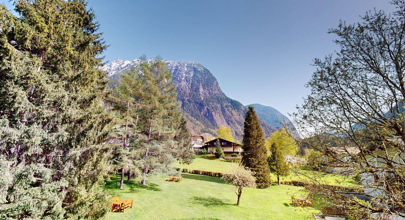 Weitläufiger Gartenbereich mit Rasenflächen, Bäumen und malerischem Bergblick unter blauem Himmel.