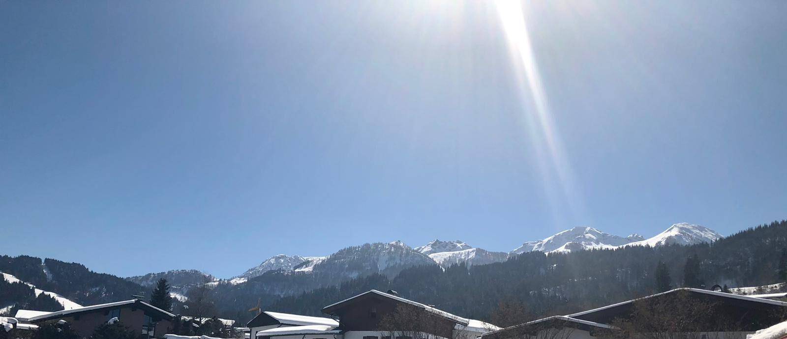 Strahlender Sonnenschein über einer verschneiten Bergkette mit klarem blauem Himmel.