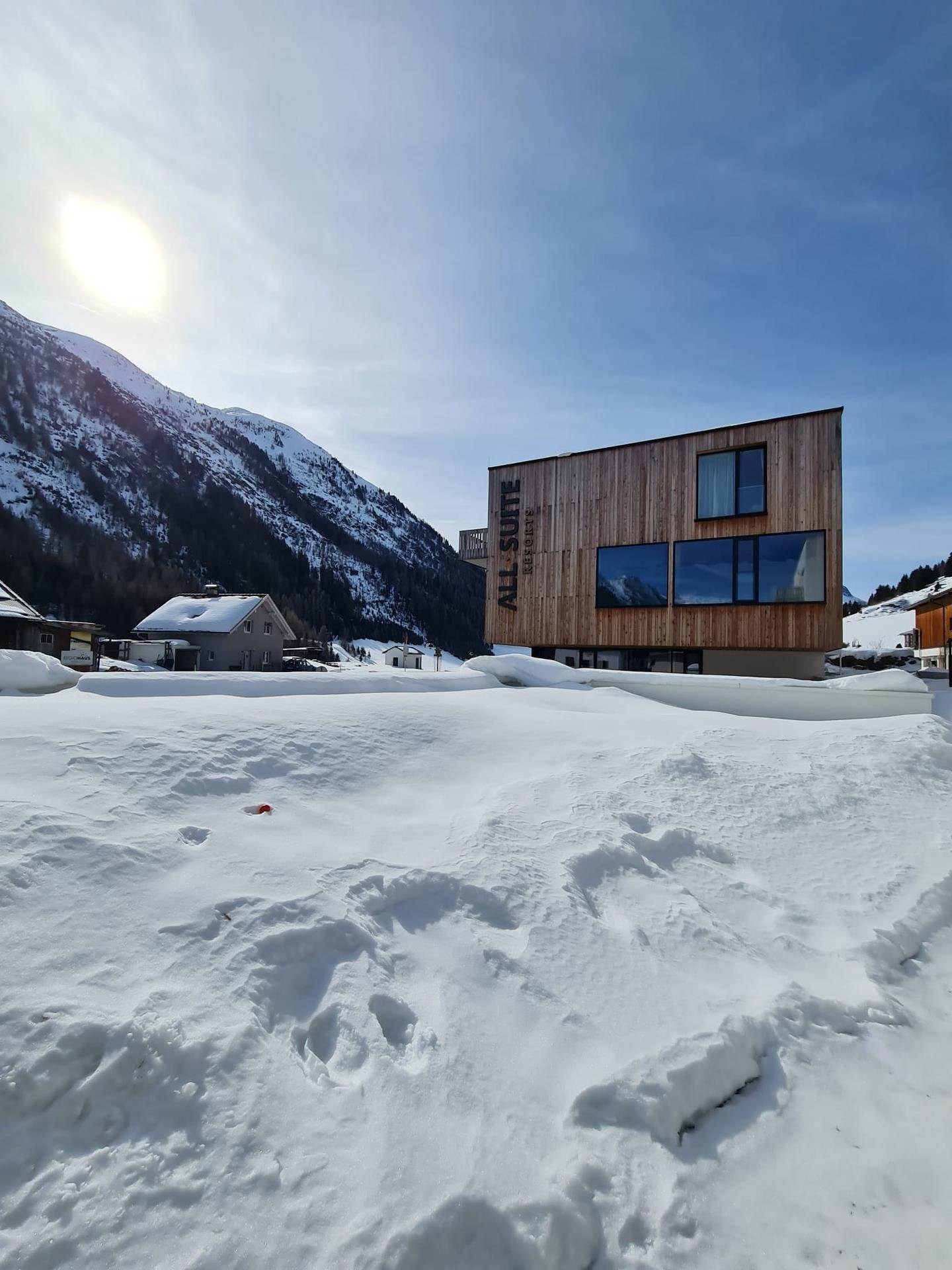 Modernes Holzgebäude in einer verschneiten Berglandschaft unter klarem Winterhimmel.
