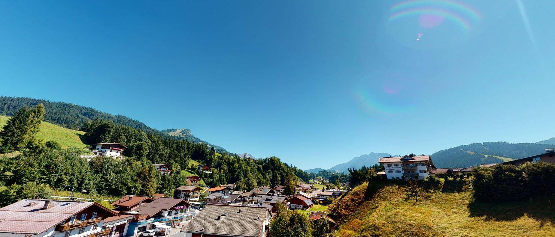 Weitläufiger Panoramablick auf grüne Berge und ein malerisches Dorf unter blauem Himmel.
