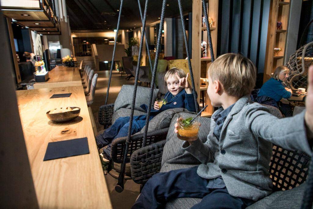 Kinder entspannen auf Schaukelsitzen in einem stilvollen, modern eingerichteten Loungebereich.