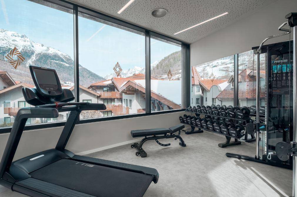 Gut ausgestatteter Fitnessraum mit modernen Geräten, großen Fenstern und inspirierendem Bergblick.